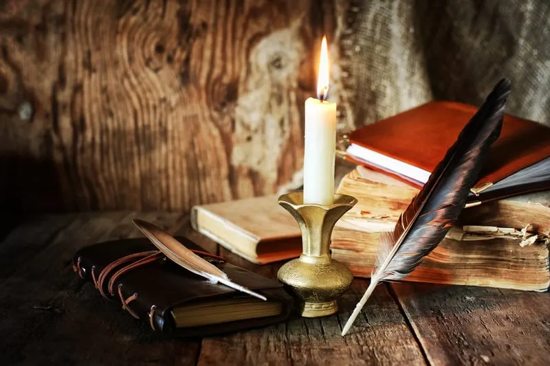 Vela, libros y una pluma de escribir